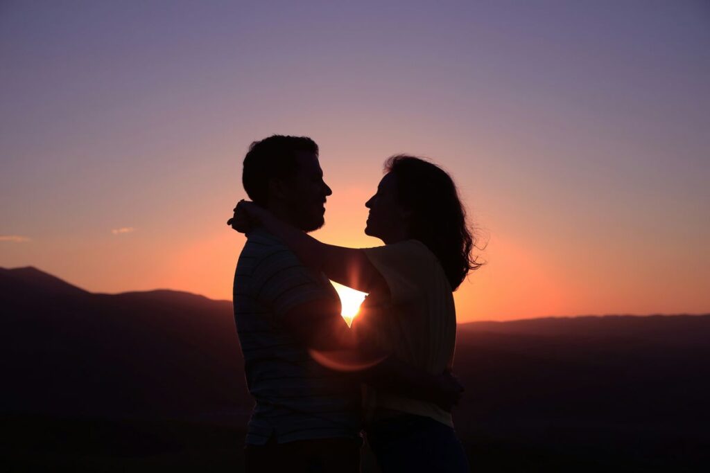 Polyamorous couple smiling at each other in front of a sunset