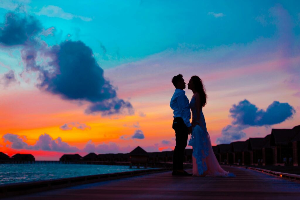 Man and Woman Wearing Wedding Attire Standing on Sea Dock during Golden Hour
