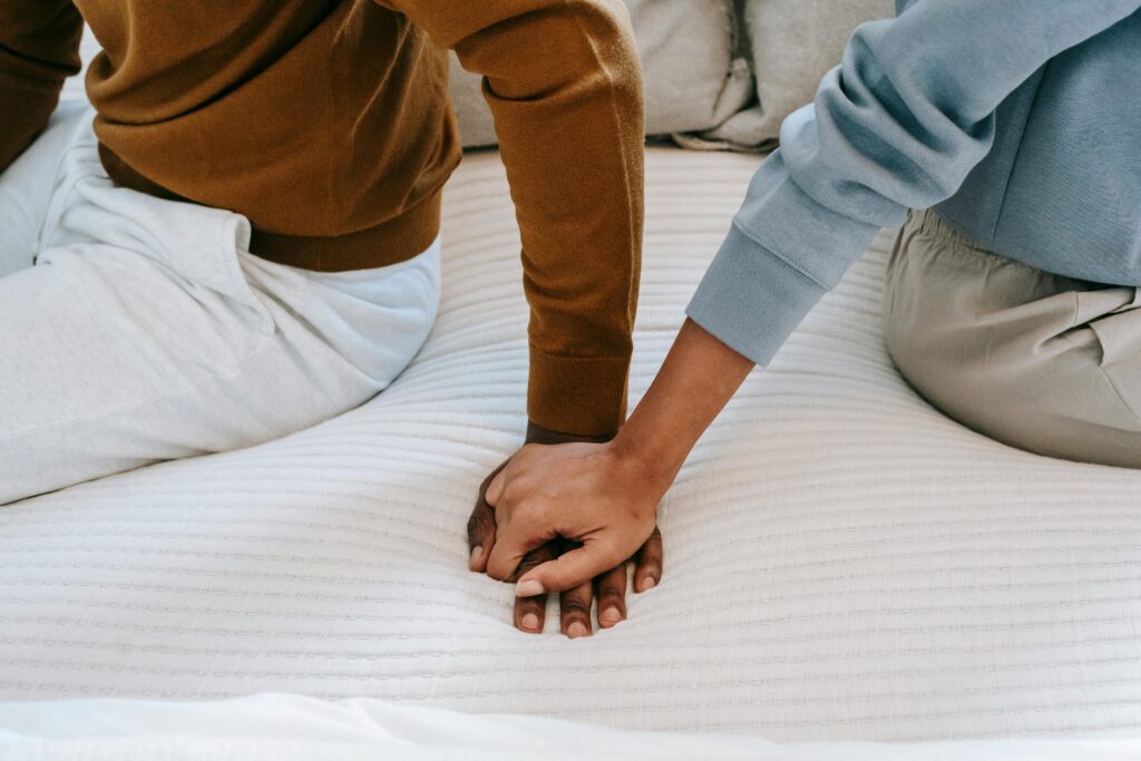 Crop unrecognizable black couple holding hands on bed
