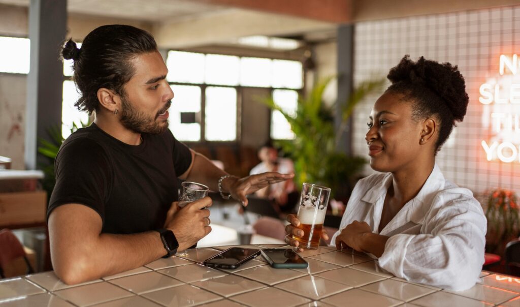 A woman and man sitting at a bar drinking beers