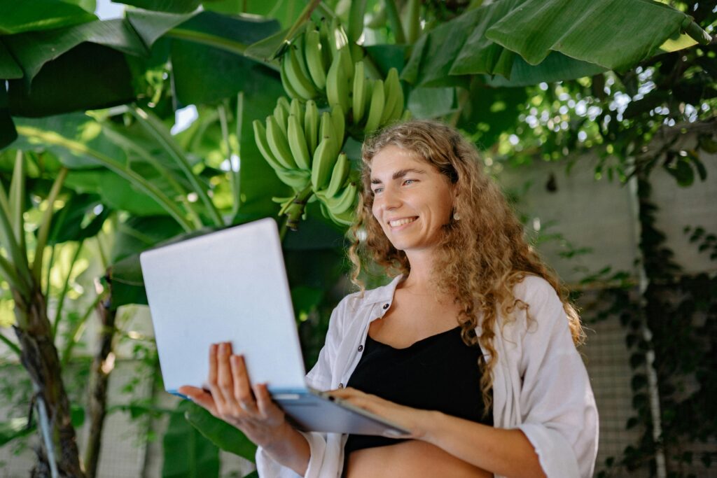 Photo of a Woman with a Laptop, Standing against a Banana Plant
