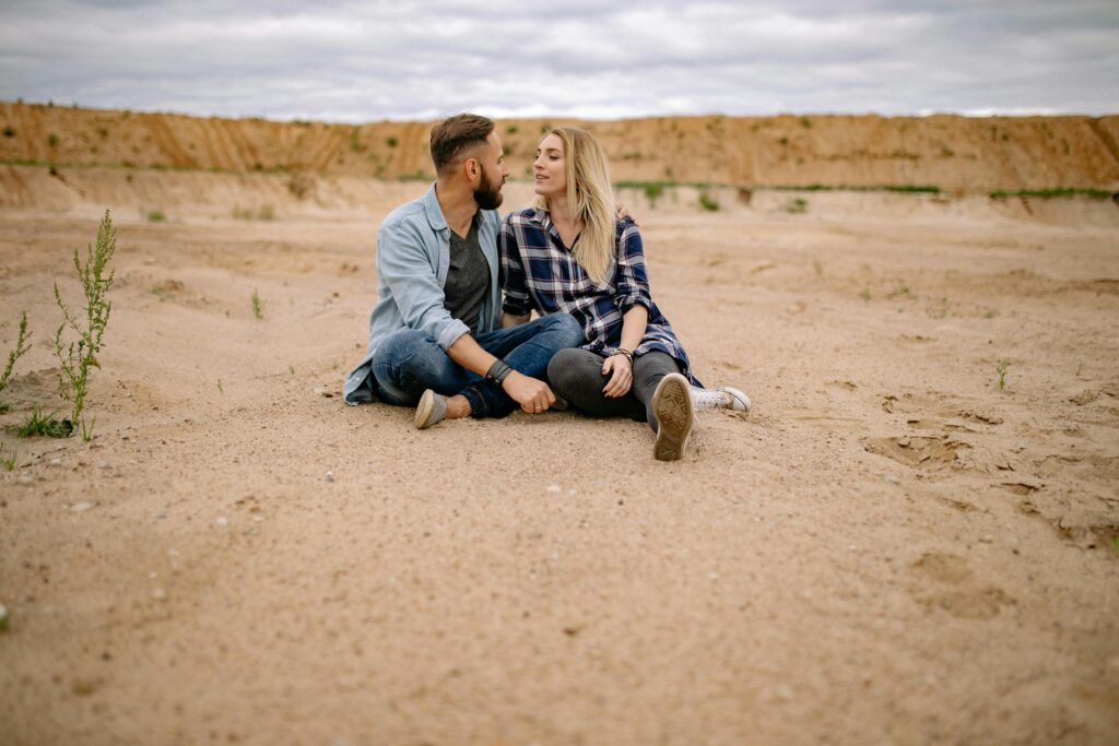 Polyamorous Couple Sitting on Sand in Desert
