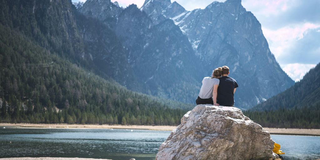 a couple sits on a rock looking out over a lake