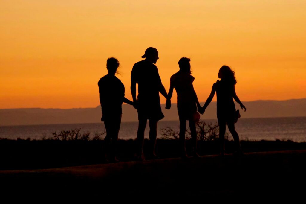 silhouette of friends standing beside shore under brown sky during daytime