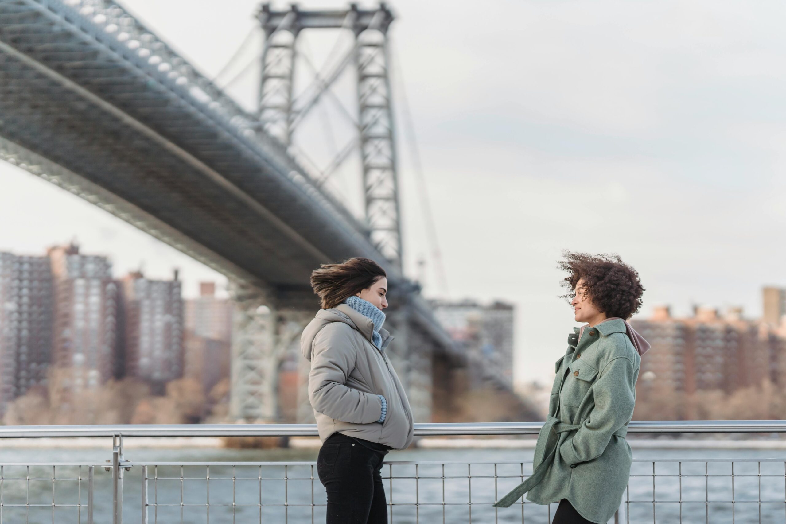 Women in outerwear chatting on city embankment on windy day